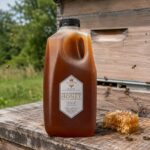 Queens Hive 6 lb raw honey jug beside beehive